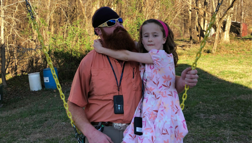 Jason Cox and his daughter Chastity sit on a swing together while wearing MegaVoice audio Bibles around their necks