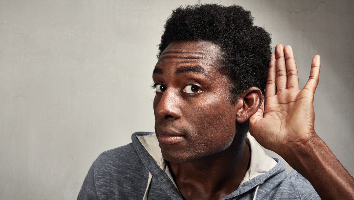 Black man leans in with hand behind ear in order to hear better.