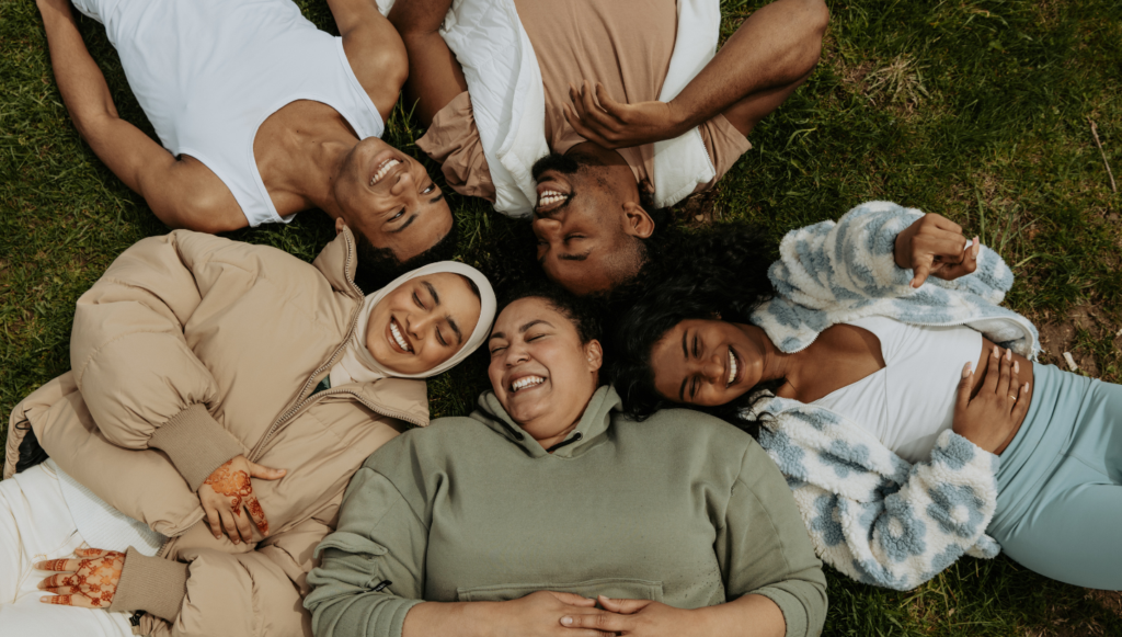 Five friends laughing together in the grass